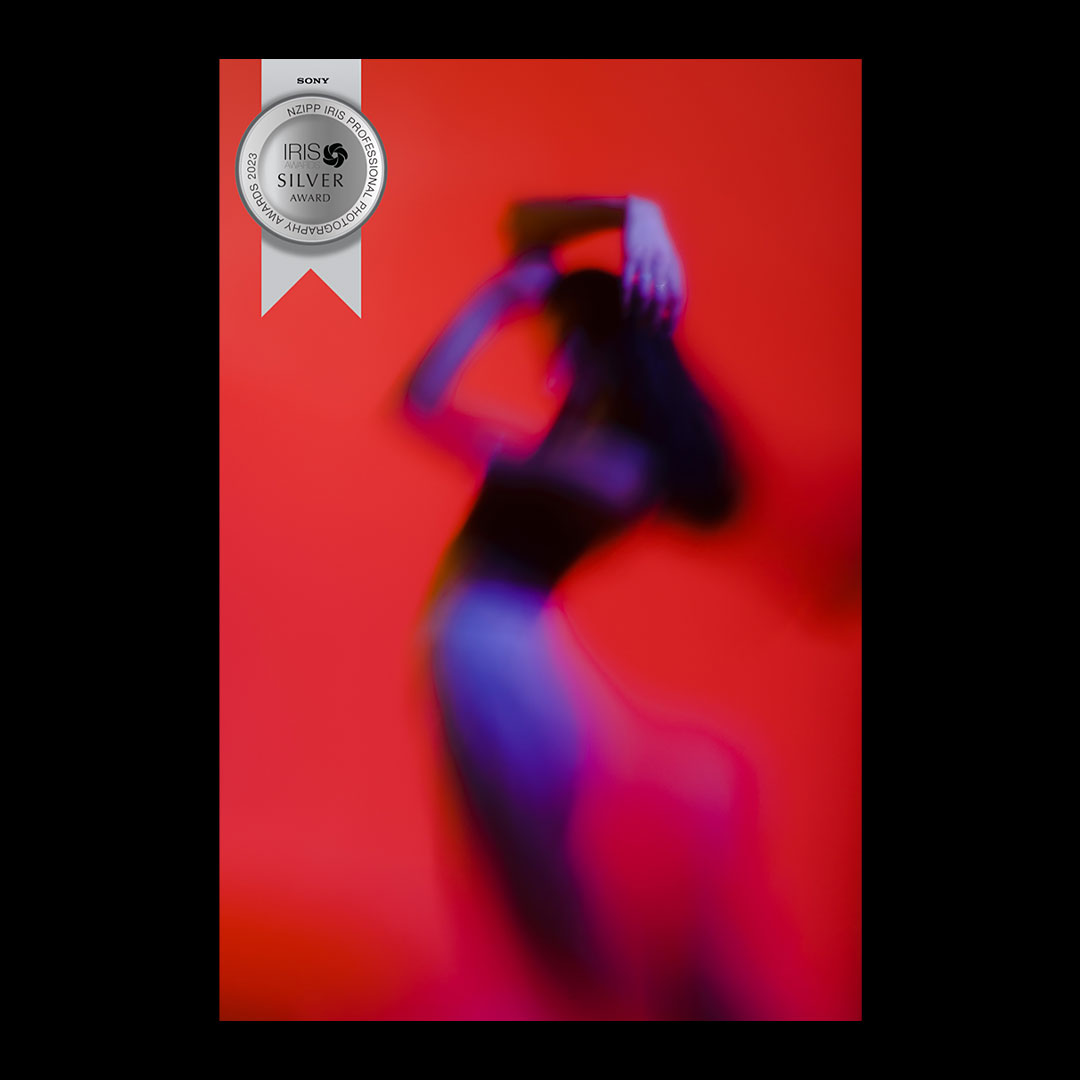 image of a female figure, posed in a twisted way with a red backdrop. the image has a silver medal overlaid depicting its status as a silver award winner at the NZIPP IRIS awards